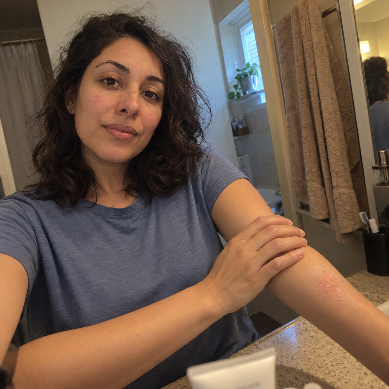 AI-generated bathroom selfie of a fictional woman in a blue shirt resting her hand on a dry forearm; not a customer result